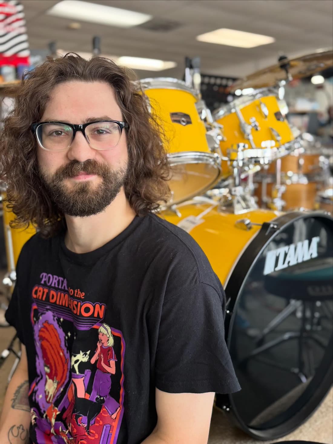 A member of the Musicians Discount Center staff in the shop, standing in front of a Tama drum kit